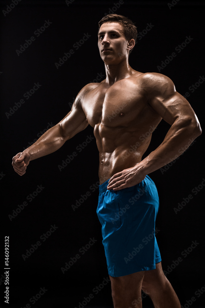 Muscular and fit young bodybuilder fitness male model posing over black background.