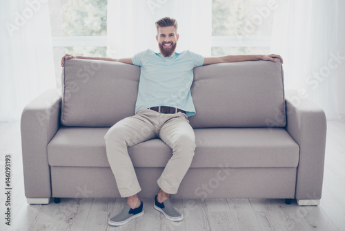 Portrait of relaxed smiling handsome bearded man resting on cozy sofa at living room at home © deagreez