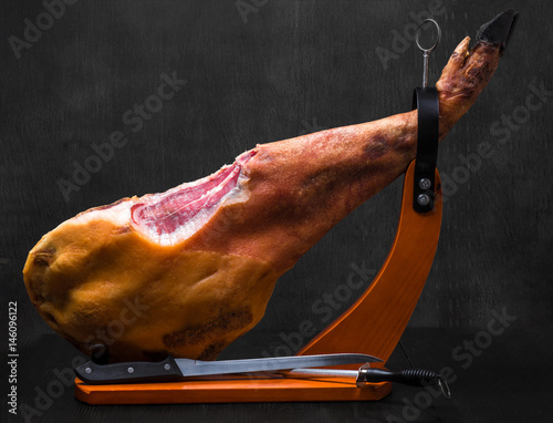Whole jamon on a wooden stand on dark background photo