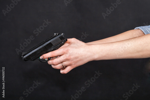 Caucasian women arms holding a gun against black background