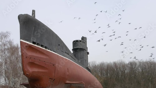 Old rusty submarine. A flock of birds flies by and sits down on the bridge deckhouse and deck. Soviet military holed ship. Vessel in front of trees in autumn and winter photo