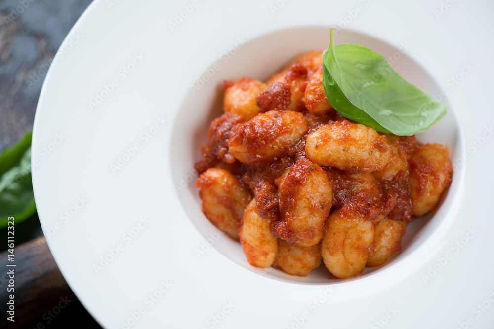 Close-up of a white plate with potato gnocchi served with red pesto sauce, horizontal shot