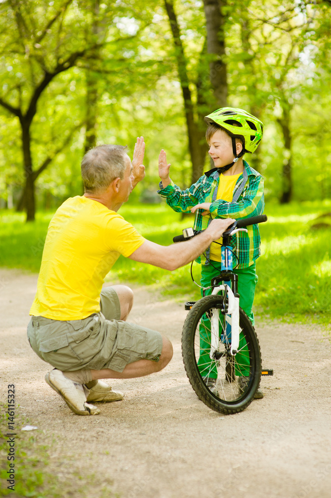 Father and son give high five while cycling in the park Father and son give high five while cycling in the park