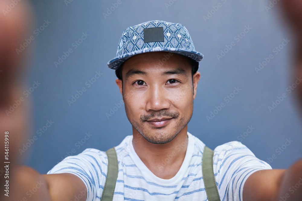 Smiling young Asian man taking a selfie outside