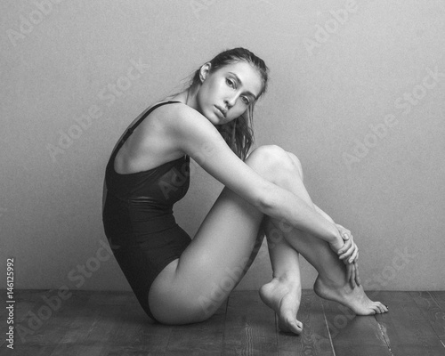 Portrait of beautiful fashion model wearing leotard while sitting on hardwood floor against wall photo