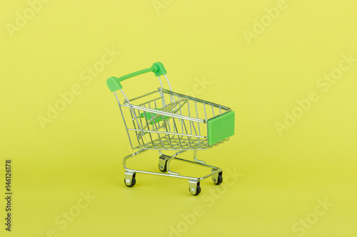 Empty miniature shopping pushcart, yellow background