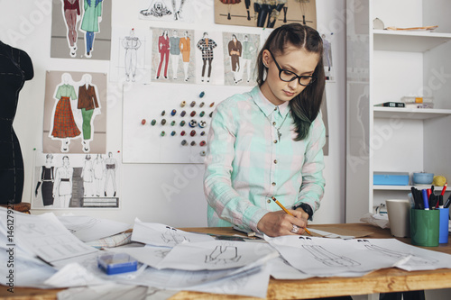 Beautiful fashion designer drawing sketch at workbench in studio