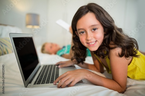 Portrait of smiling girl using laptop on bed in bedroom