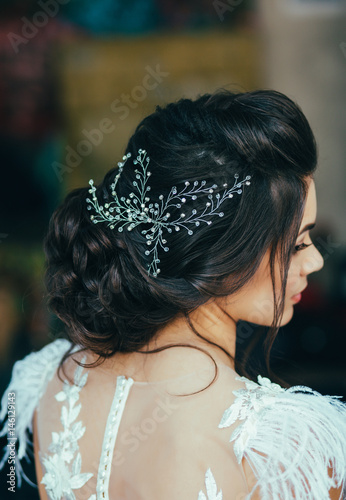 Elegant brunette bride sitting back with collected hair. Tender wedding stylish hairstyle with accessories.
