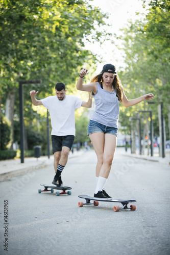 Happy young couple having fun with skateboard on the road. Young man and woman skating together.