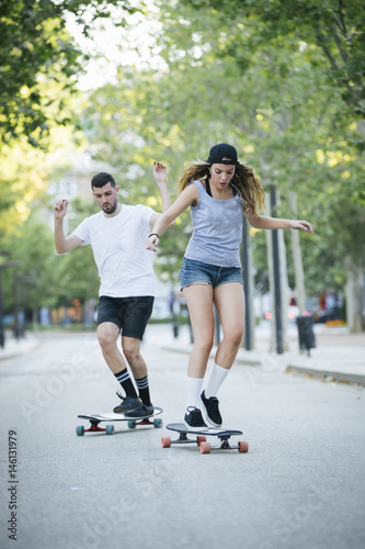 Happy young couple having fun with skateboard on the road. Young man and woman skating together. © juananbarros