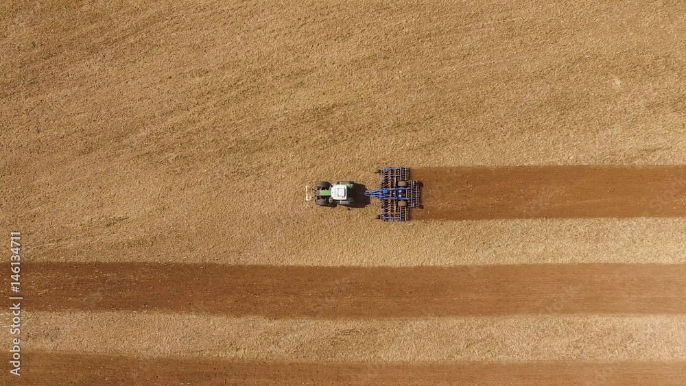 Fototapeta aerial view of a tractor at work on agricultural fields - tractor cultivating a field in spring