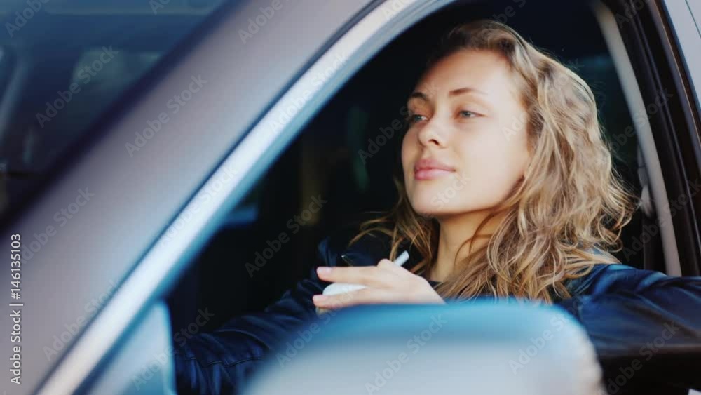 Portrait of a young woman sitting in the car and drinking coffee from a paper cup. Looks at the open window, admiring something Portrait of a young woman sitting in the car and drinking coffee from a paper cup. Looks at the open window, admiring something