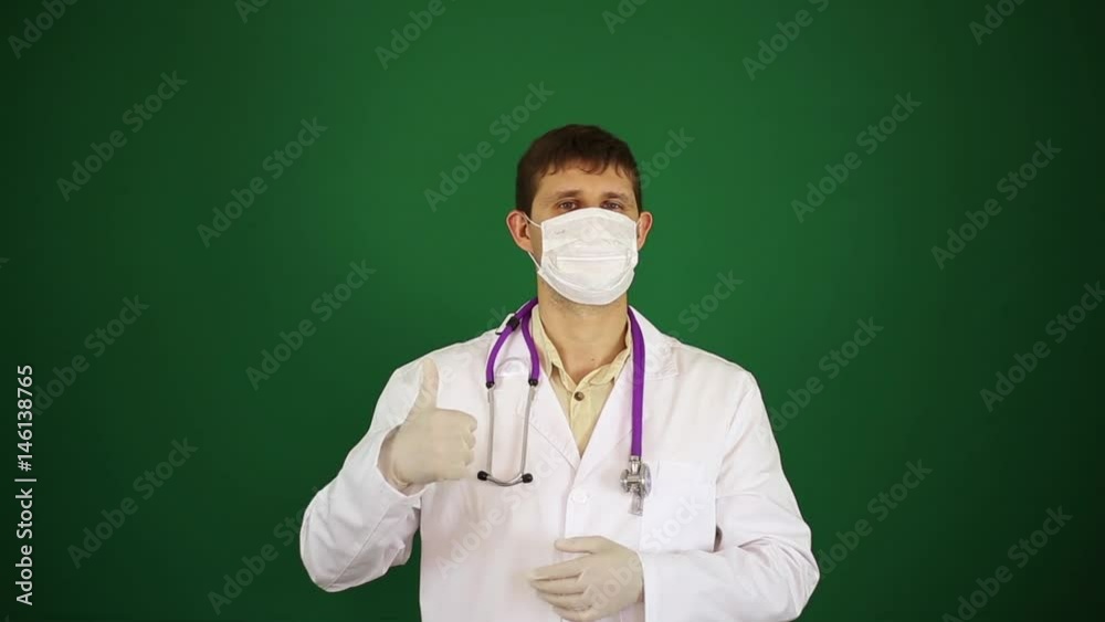 Doctor in medical mask shows thumbs up. Doctor on green background shows thumb up. Doctor in medical mask shows thumbs up. Doctor on green background shows thumb up.
