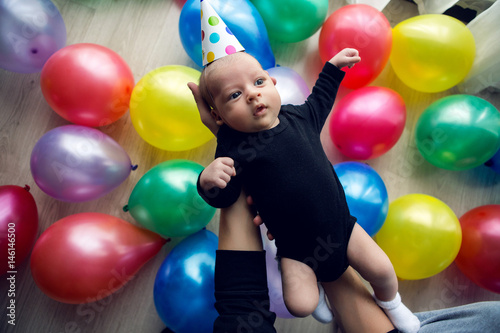 child in a festive cap in polka-dot lies on his hands against the background of colorful balloons