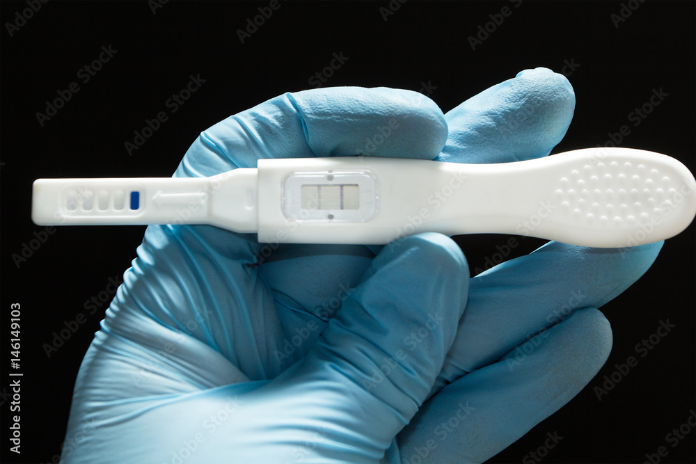 artificial insemination. Positive pregnancy test with two strips in the hand a blue medical glove a black background. Stock-foto Adobe Stock