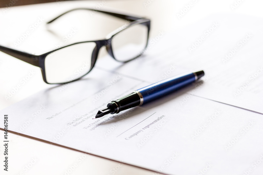 Signing the contract with pen and glasses in business work on office desk Signing the contract with pen and glasses in business work on office desk