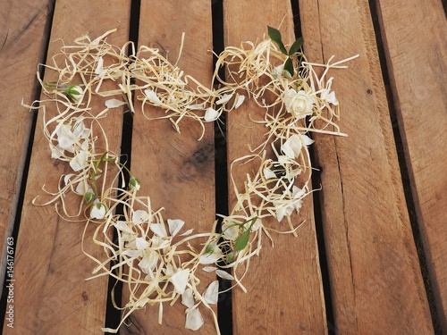 Coração de palha e petalas de rosinhas brancas visto de cima sobre Palete de madeira rústica photo