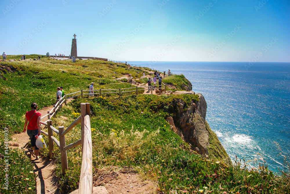 People walking down the path on the edge of the cliff in Cape Roca, Portugal with view of Atlantic ocean