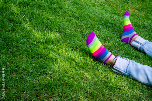 Legs laying on the green grass with colorful socks. Person resting on the floor in the park.
