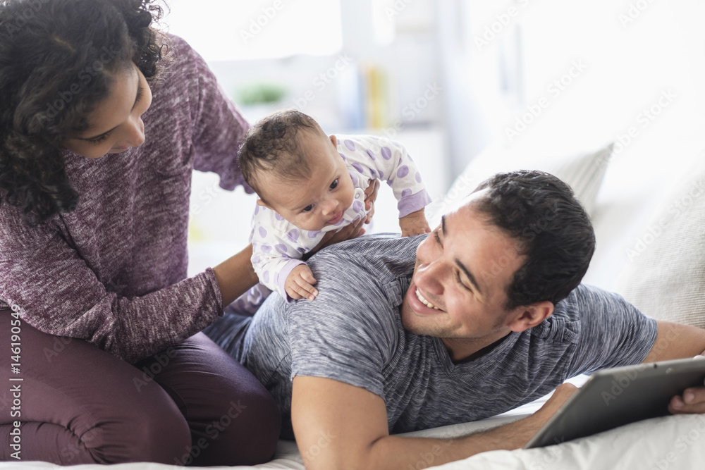 Hispanic mother holding baby daughter on back of father Hispanic mother holding baby daughter on back of father