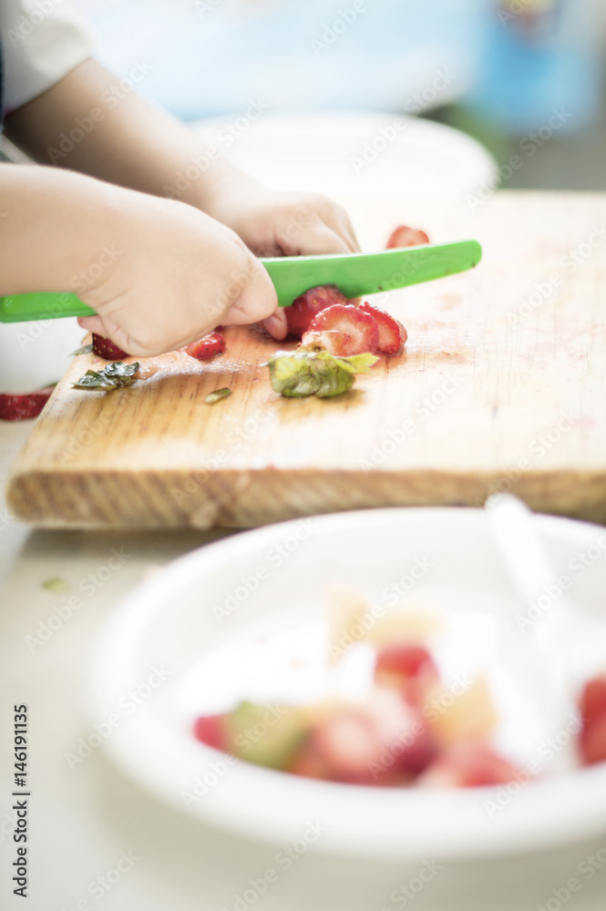Hands of Hispanic boy cutting strawberry with plastic knife