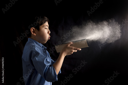 Boy blows dust off book.