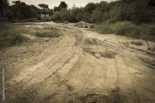 sepia wheel trail on a muddy ground with abandoned house in wilderness