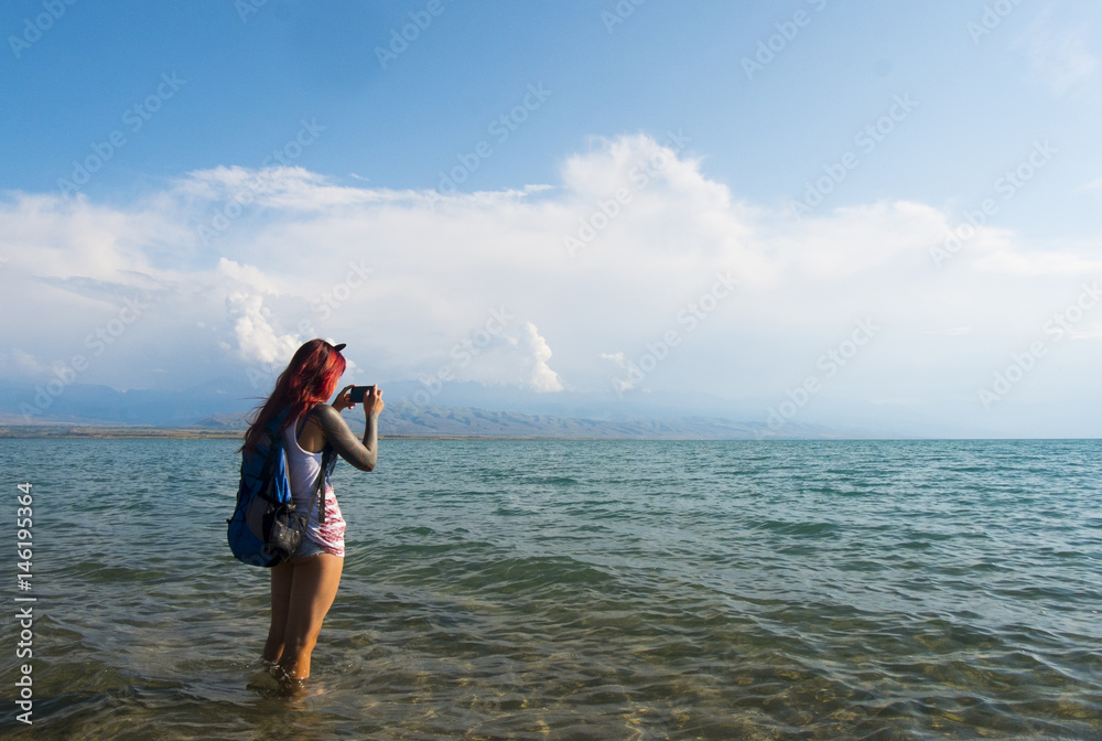 Caucasian woman wading in ocean photographing with cell phone Caucasian woman wading in ocean photographing with cell phone