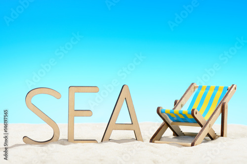 The word SEA and sunbed at the beach on background of blue sky