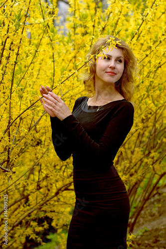 Attractive young sexy woman in a black dress in a botanical garden looks at a yellow plant that comes with a pleasant walk and a visit surrounded by plants