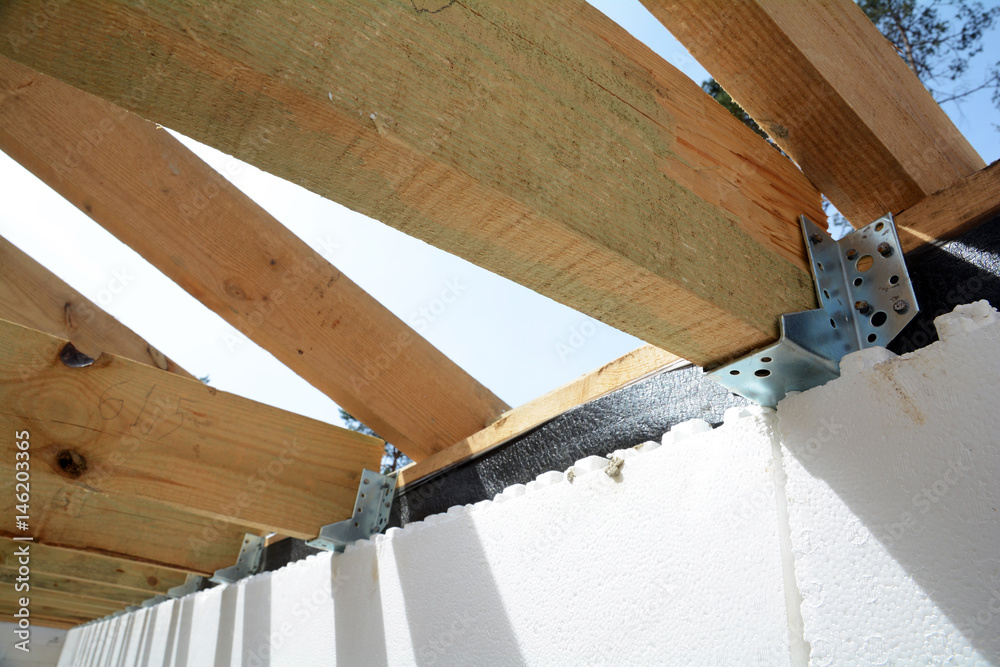 Obraz premium The wooden structure of the building. Wooden frame building. Wooden roof construction. house building. Installation of wooden beams at construction the roof truss system of the house.