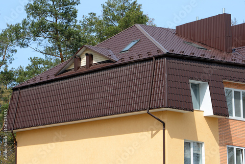 Dormer windows on metal roof. A house with a roof made of metal roofing with mansard windows and rain gutter.