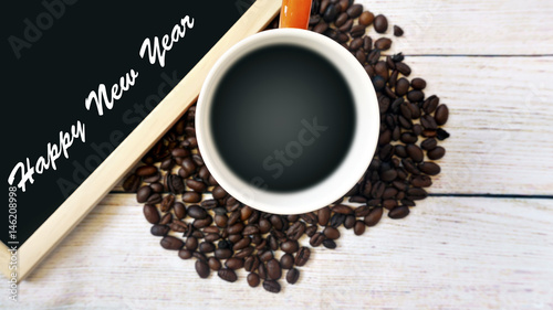 Fototapeta Naklejka Na Ścianę i Meble -  Heat a cup of coffee, coffee beans and a whiteboard with the word HAPPY NEW YEAR