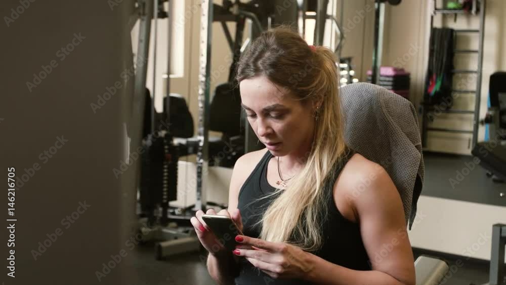 tired 20s blonde sportswoman after exercise chatting with smartphone in a gym tired 20s blonde sportswoman after exercise chatting with smartphone in a gym
