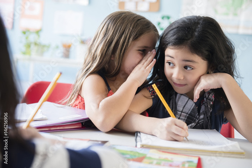 Girl whispering to classmate in school