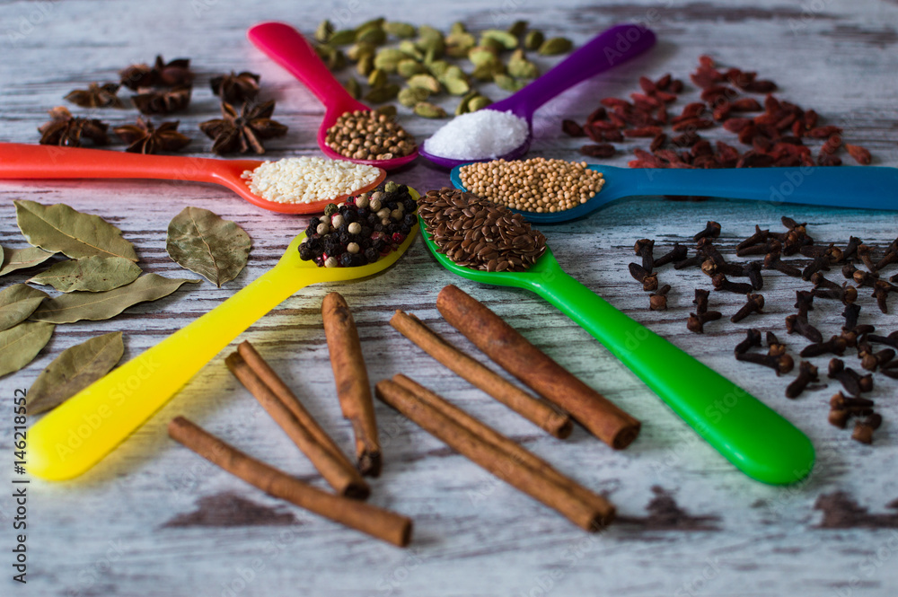 Black pepper, cardamom, coriander, mustard seeds, bay leaf, cinnamon, anise, goji berries, salt, sesame and cloves in the colorful spoons in the form of a circle.