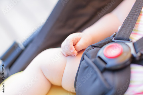 Close-up of newborn baby hand while sleeping in stroller outdoors. Red button of fasten seat belt. Focus on cute fingers.