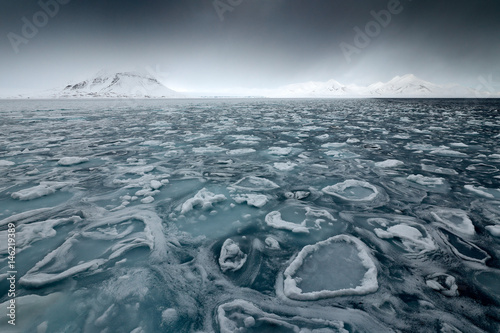 Land of ice. Winter Arctic. White snowy mountain, blue glacier Svalbard, Norway. Ice in ocean. Iceberg in North pole. Black clouds with ice floe. Beautiful landscape. Cold sea water.