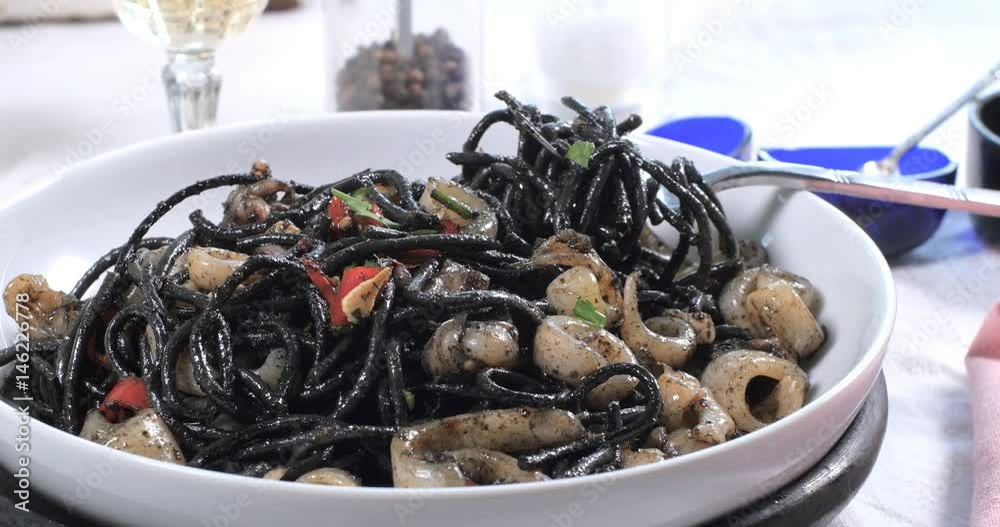 Sprinkling parsley over black pasta with squids (cuttlefish) and ink Sprinkling parsley over black pasta with squids (cuttlefish) and ink