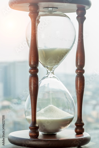 Vintage style of white sand crystal and wooden hourglass with blurred city view in background.