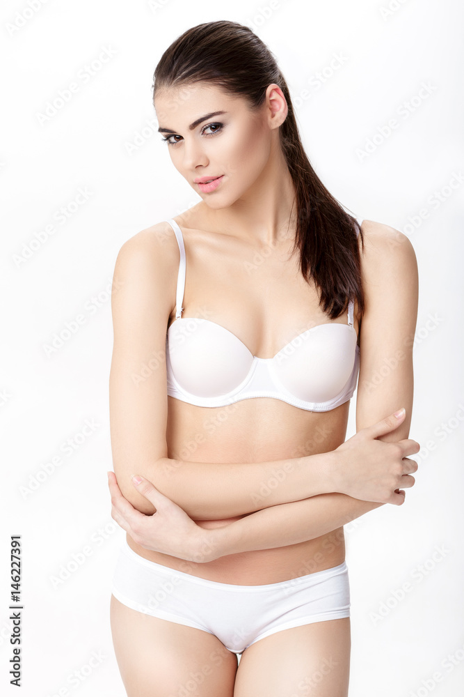 Obraz premium beautiful young brunette woman with perfect sporty body in white underwear on white background