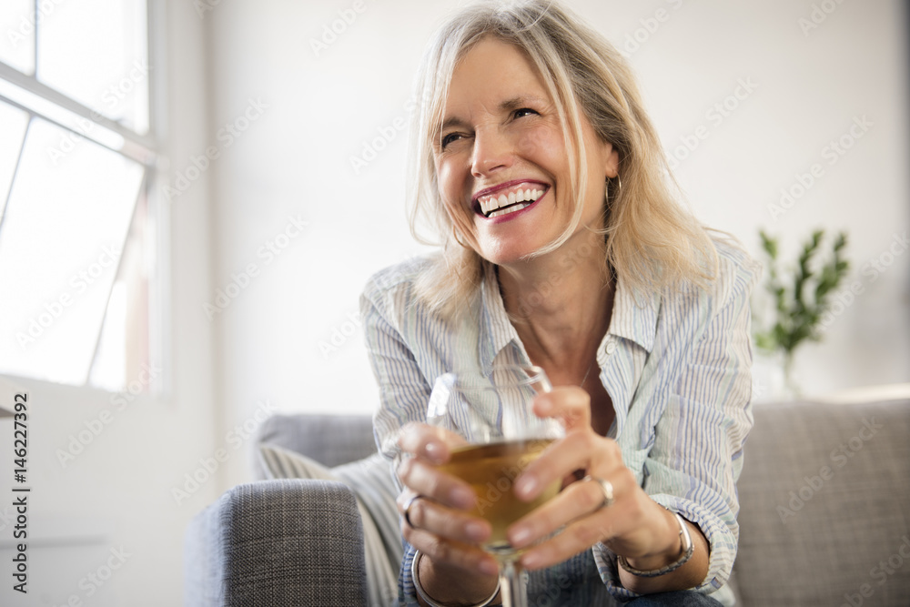 Smiling Caucasian woman sitting on sofa drinking white wine Smiling Caucasian woman sitting on sofa drinking white wine