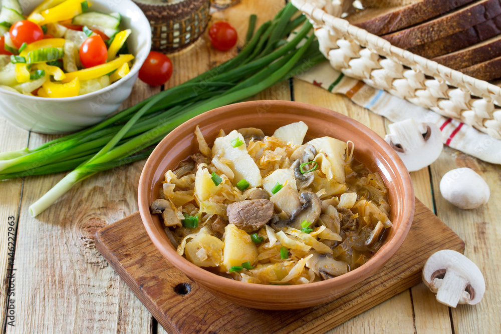 Stewed cabbage with mushrooms, mushrooms and tomato sauce with fresh vegetables on a wooden table.