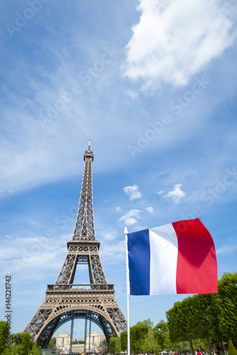 French tricolour flag flying in bright blue sky on a summer day in front of the Eiffel Tower in Paris, France