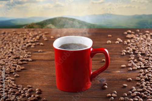 Red cup of hot coffee on a wooden background, on a background of mountains. Smoking coffee, steaming