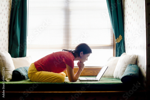 Japanese woman leaning on day bed reading laptop photo