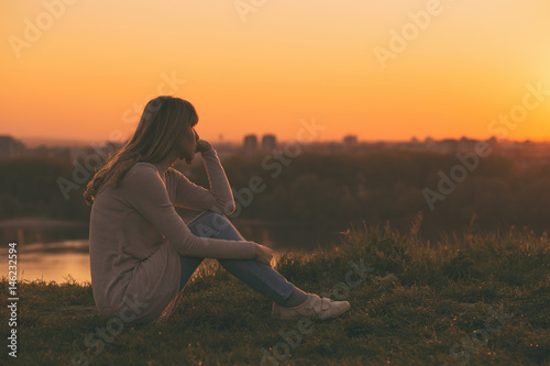 Sad woman sitting at the sunset and thinking.