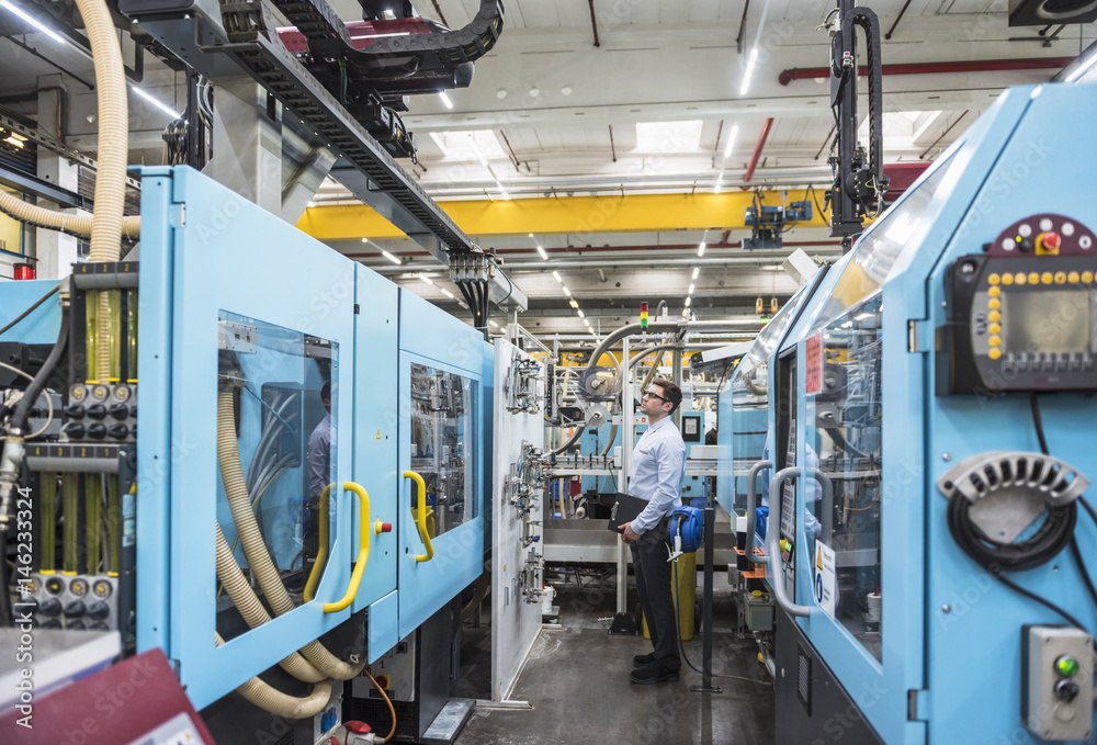 Man with documents standing among machines in factory shop floor