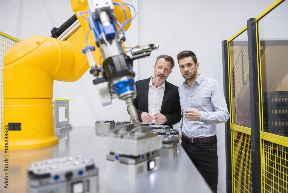 Two businessman observing industrial robots in factory Two businessman observing industrial robots in factory